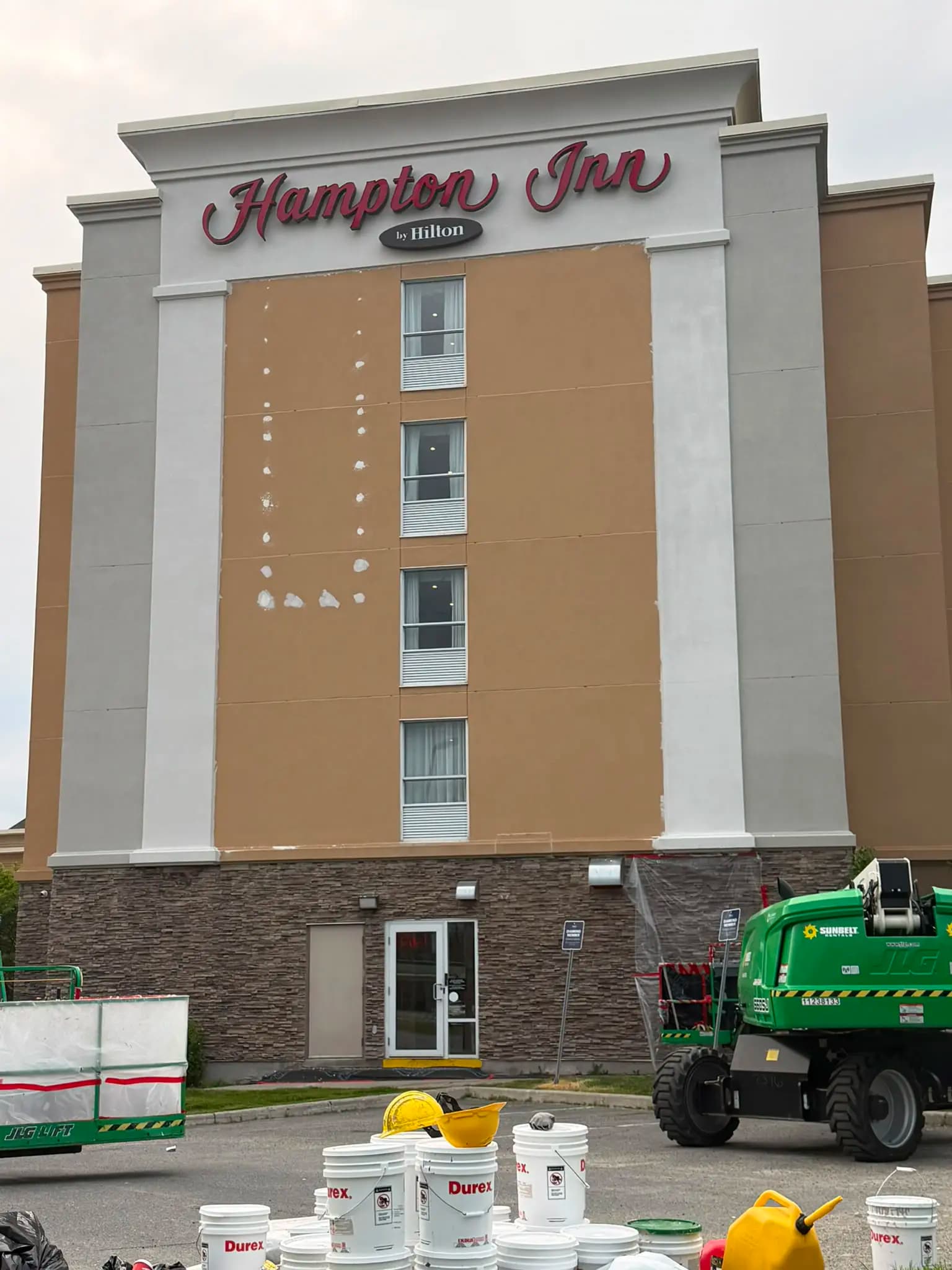 Hampton Inn, Greater Sudbury — Patch repairs across the field under the rooftop sign, material staged below